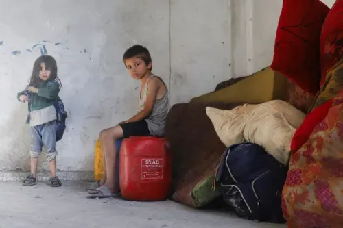 طفلان فلسطينيان يجلسان في مكان مهدم، حيث يبدو أن الفقر والمعاناة تؤثر عليهما، مع وجود أكياس وأثاث متهالك حولهما.