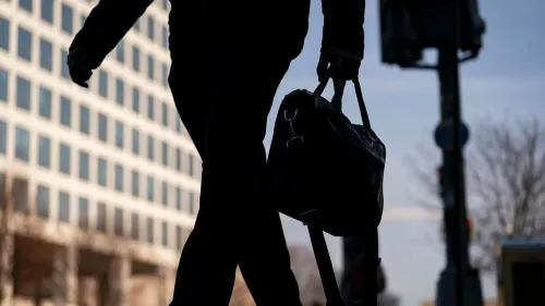 شخص يسير في الشارع حاملاً حقيبة، مع خلفية لمباني تجارية في واشنطن، يعكس تأثير تسريح العمال على الاقتصاد المحلي.