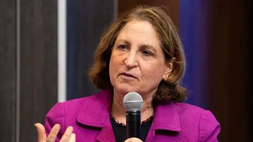 تظهر روث ماركوس، الكاتبة السابقة في واشنطن بوست، وهي تتحدث في حدث، مرتدية سترة بنفسجية وتحمل ميكروفونًا، معبرة عن آرائها حول تغييرات بيزوس في الصحيفة.