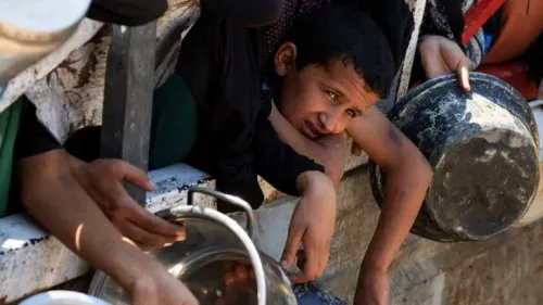 طفل فلسطيني يبدو عليه التعب والقلق، يمد يده من بين حشود للحصول على الطعام، مع تزايد حالات سوء التغذية في غزة.