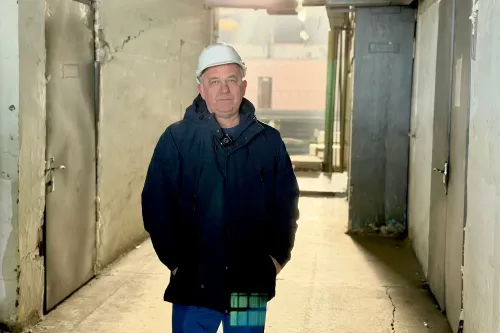 أولكسندر أداموف يقف في ممر منشأة الطاقة الأوكرانية، مرتديًا خوذة وسترة، بينما تتعرض المنشأة لهجمات متكررة من روسيا.