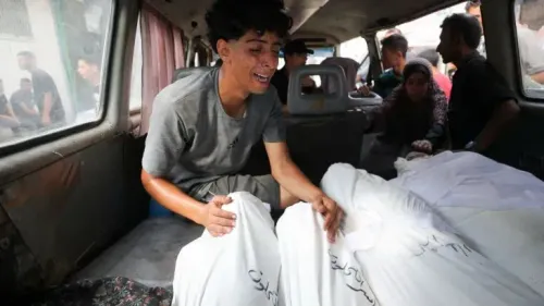 شاب يبكي بجانب جثث مغطاة بأكفان بيضاء داخل سيارة إسعاف في غزة، معبرًا عن الحزن العميق بسبب فقدان أحبائه في الأحداث الجارية.