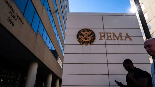 مبنى إدارة الطوارئ الفيدرالية (FEMA) مع شعار الوزارة، ويظهر فيه أشخاص يسيرون أمامه، مما يبرز تأثير الأزمات على الوكالة.