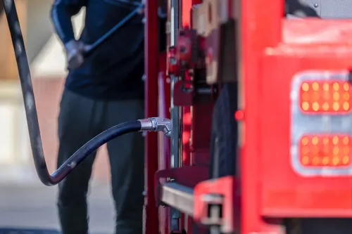 تظهر الصورة شخصًا يقوم بتعبئة الوقود في مضخة بنزين، مع التركيز على الخرطوم والمضخة، مما يعكس تأثير ارتفاع أسعار البنزين على الاقتصاد.