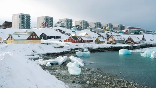 منظر لمدينة غرينلاند، يظهر المنازل الملونة التقليدية وسط الثلوج والمباني الحديثة، مع الجليد العائم في المياه.