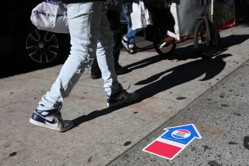 أشخاص يسيرون على الرصيف بالقرب من علامة تشير إلى التصويت، تعكس أهمية المشاركة في الانتخابات المقبلة في نيويورك.