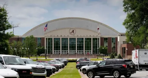 واجهة كوليسيوم جامعة ألاباما، حيث أقيم حفل التخرج، مع العلم الأمريكي وعلم الولاية، ومركبات متوقفة في المقدمة.