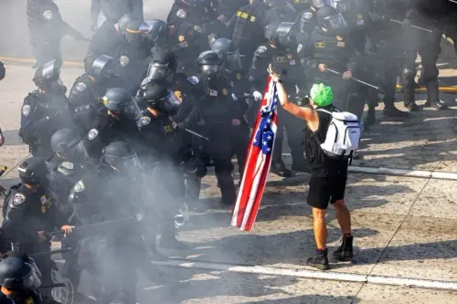 محتج يحمل علم الولايات المتحدة وسط دخان الغاز المسيل للدموع، يواجه صفوفًا من الشرطة المدججة بالسلاح في لوس أنجلوس.