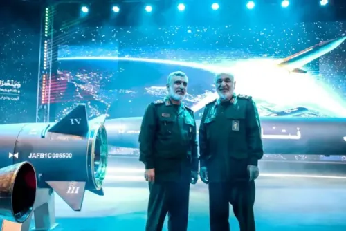 جنرالان إيرانيان يرتديان زي الحرس الثوري الإسلامي، يقفان أمام صاروخ بحضور خلفية مضيئة، في سياق التوترات العسكرية المتصاعدة.