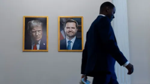 صورة رسمية للرئيس ترامب تظهر تعبيرًا جادًا، مع خلفية داكنة ودبوس علم أمريكي، بينما يمر شخص يرتدي بدلة.