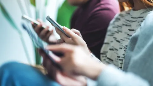 شباب ومراهقون يستخدمون هواتفهم المحمولة، يعكسون موضوع الدراسة حول تأثير تحذيرات الصحة النفسية على تقليل إدمان وسائل التواصل الاجتماعي.