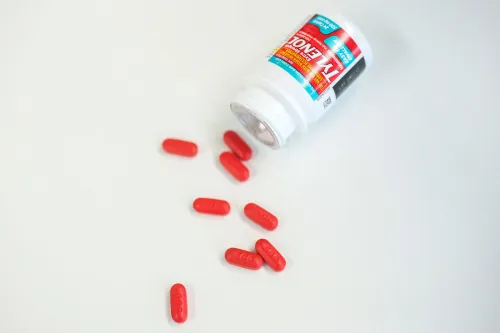 عبوة تايلينول مفتوحة مع حبوب حمراء متناثرة حولها، تشير إلى النقاش حول سلامة استخدام الأسيتامينوفين أثناء الحمل.