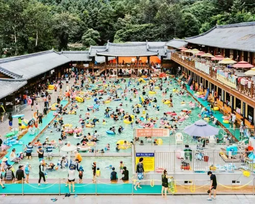 حمام سباحة مزدحم في كوريا الجنوبية، حيث يستمتع الناس بالاسترخاء واللعب، مع خلفية معمارية تقليدية تعكس ثقافة الترفيه المعاصرة.