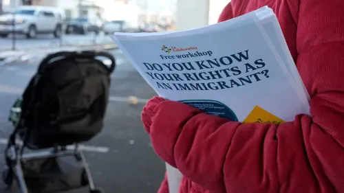 ورقة تحمل عنوان "هل تعرف حقوقك ك immigrant؟" ممسكة بها شخص يرتدي سترة حمراء، مع عربة أطفال في الخلفية، في سياق ورشة عمل حول حقوق المهاجرين.