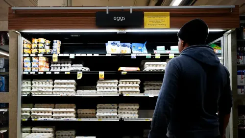 رجل يتطلع إلى رف البيض في متجر، حيث الأسعار مرتفعة والنقص يبدو واضحًا، مما يعكس تأثير التضخم على المتسوقين.