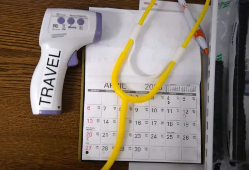 أداة قياس الحرارة الرقمية بجانب تقويم شهري يظهر شهر أبريل، مع سماعة طبية وأقلام، تعكس الاستعدادات لمواجهة تفشي الحصبة.