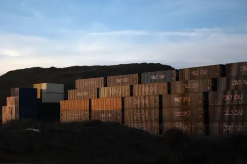 صناديق شحن متعددة الألوان مكدسة في موقع مفتوح تحت سماء زرقاء، تعكس تأثير التعريفات الجمركية على التجارة الأمريكية.