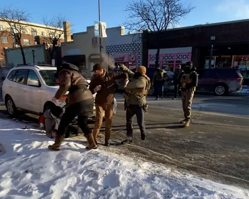 تظهر الصورة لحظة من حادثة إطلاق نار في مينيابوليس، حيث يتصارع ضباط الهجرة مع رجل على الأرض وسط حشود من المتظاهرين.