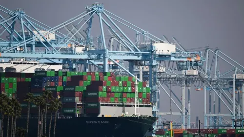 صورة لميناء مزدحم بالحاويات والسفن، حيث تُظهر الرافعات الكبيرة والمعدات المستخدمة في تحميل وتفريغ البضائع، مما يعكس تأثير التعريفات الجمركية على التجارة.