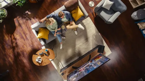 زوجان يجلسان على أريكة في غرفة معيشة مريحة، يشاهدان التلفاز مع وعاء من الفشار، يعكسان شعور الراحة والأمان المالي.