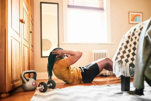شخص يمارس تمارين البطن في غرفة مع أثاث خشبي وأوزان، مما يعكس أهمية النشاط البدني في تعزيز عملية الأيض وفقدان الوزن.