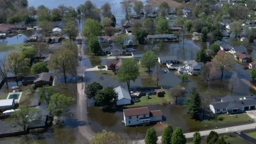 مناطق سكنية غارقة بالمياه بعد الفيضانات، مع منازل وأشجار محاطة بالمياه، تعكس تأثير الكوارث الطبيعية على المجتمعات.