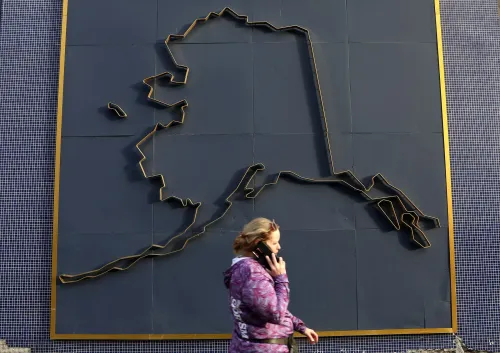 امرأة تتحدث على الهاتف أمام لوحة جدارية توضح خريطة ولاية ألاسكا، في سياق التحضيرات لقمة ترامب وبوتين.