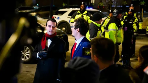 رجلان يرتديان ملابس أنيقة، أحدهما يرتدي سترة زرقاء مع ربطة عنق حمراء، يتحدثان وسط حشد من رجال الشرطة في موقع مظاهرة.