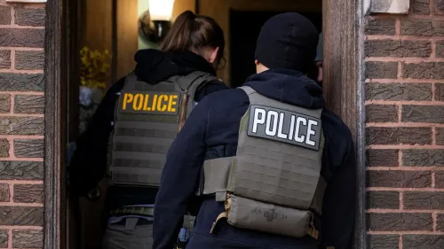 رجال شرطة يرتدون سترات تحمل كلمة "شرطة" أثناء دخولهم منزل، في إطار جهود تنفيذ سياسات الهجرة الجديدة.