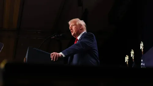 تظهر الصورة الرئيس السابق ترامب أثناء إلقائه خطابًا، حيث يتحدث إلى الجمهور وسط أجواء رسمية، مع وجود علم خلفه.