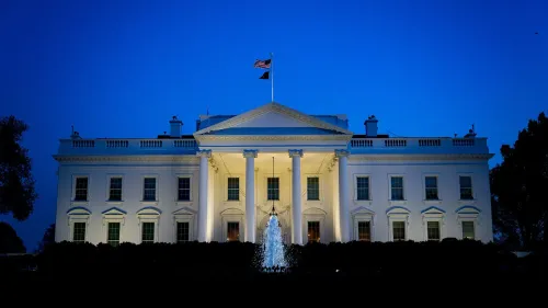 البيت الأبيض مضاء في المساء، مع العلم الأمريكي يرفرف فوقه، مما يعكس الجدل حول أصول فيروس كورونا والتسريبات المخبري.