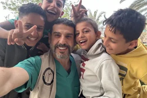 آدم حمّاوي، الجرّاح المتخصص في جراحة التجميل، يبتسم مع مجموعة من الأطفال في غزة، معبراً عن الأمل والشجاعة في مواجهة التحديات.