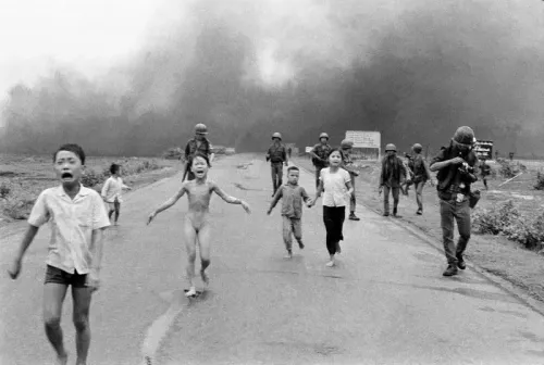 صورة تاريخية تظهر أطفالًا يهربون من هجوم بالنابالم خلال حرب فيتنام، مع جنود في الخلفية، تعكس مأساة الحرب وأثرها على المدنيين.