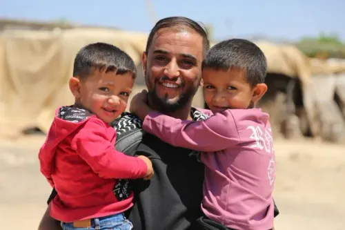 عودة الهذالين يحتضن طفليه في مسافر يطا، الضفة الغربية، حيث يُظهر الصورة حبه العميق لعائلته وسط تحديات الاحتلال.