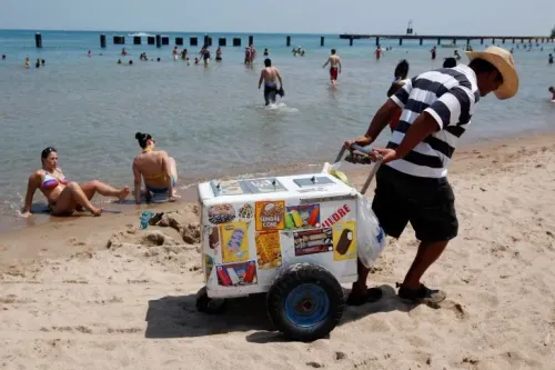 بائع آيس كريم يدفع عربة محملة بالمثلجات على شاطئ مزدحم، حيث يستمتع الناس بالسباحة في البحر.