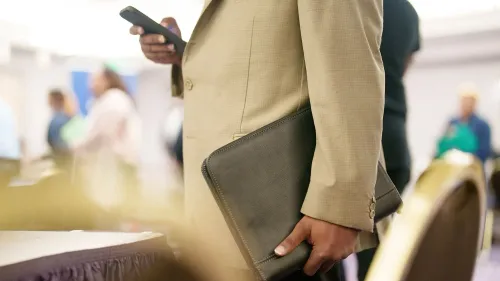 رجل يرتدي بدلة يحمل حقيبة مستندات وهاتفًا محمولًا، في سياق مناقشات حول البطالة بين الأمريكيين السود.