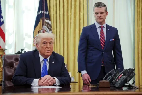 ترامب يجلس خلف مكتبه في المكتب البيضاوي بينما يقف هيغسيث خلفه، مما يعكس العلاقة بينهما في سياق الأمن القومي.