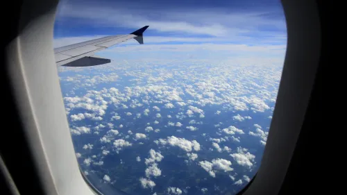 من نافذة طائرة، يظهر جناح الطائرة فوق سحب بيضاء وكثيفة، مع سماء زرقاء صافية في الخلفية، مما يعكس تجربة السفر الجوي.