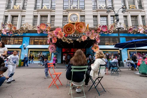 واجهة متجر Macy's مزينة بأزهار ملونة، مع زبائن يجلسون في الخارج وأطفال يلعبون، تعكس الانتعاش في مبيعات الشركة.