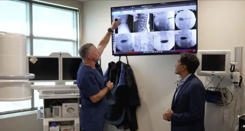 طبيب يشرح صور الأشعة على الشاشة لمريض في عيادة طبية، مع التركيز على استراتيجيات جديدة لتخفيف الألم.