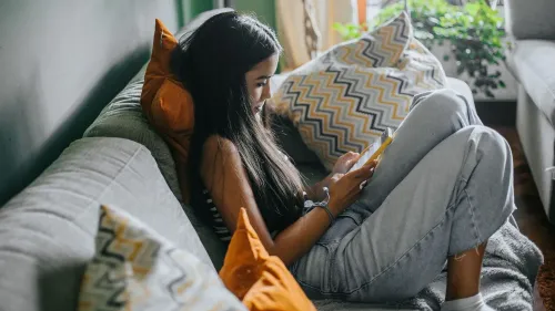 فتاة مراهقة تجلس على الأريكة، تحمل هاتفًا ذكيًا، محاطة بوسائد، تعكس التركيز على استخدام وسائل التواصل الاجتماعي وتأثيره على اضطرابات الأكل.