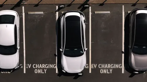 سيارات كهربائية متوقفة في موقف مخصص للشحن، مع وجود لافتة تشير إلى "شحن EV فقط"، مما يعكس أهمية الدعم الحكومي لصناعة السيارات الكهربائية.
