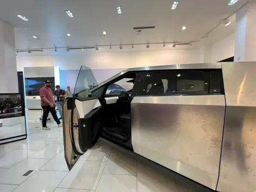 سيارة تسلا الكهربائية الجديدة ذات التصميم الفريد، مع باب مفتوح، في صالة عرض حديثة، حيث يتواجد زوار يتفقدون السيارة.