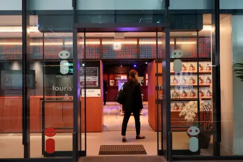 مدخل كشك معلومات سياحية حديث في طوكيو، حيث تظهر امرأة تدخل بينما تعرض الجدران كتيبات سياحية متنوعة.