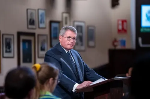 رجل يرتدي بدلة رسمية يتحدث من منصة، مع وجود صور لأشخاص خلفه، في سياق نقاش قانوني حول تأثير القضاة على السلطة.