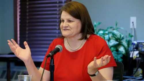 القاضية هانا دوغان تتحدث أثناء مؤتمر صحفي، مرتدية فستانًا أحمر، معبرة عن استيائها من اعتقالها بسبب قضايا تتعلق بالهجرة.