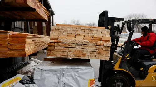 عمال يقومون بنقل كتل خشبية باستخدام رافعة شوكية، مما يعكس أهمية الخشب في التجارة بين الولايات المتحدة وكندا.