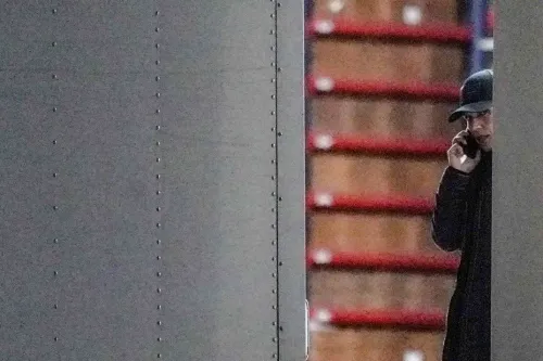 شخص يرتدي قبعة ويتحدث عبر الهاتف، يظهر جزئيًا خلف حائط معدني، مع خلفية تحتوي على صناديق خشبية، مما يعكس أجواء مرتبطة بالانتخابات.