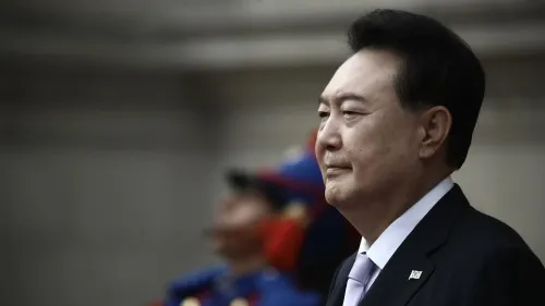 يون سوك يول، الرئيس الكوري الجنوبي السابق، يظهر بملابس رسمية خلال حدث رسمي، مع خلفية جنود يرتدون زيًا عسكريًا.