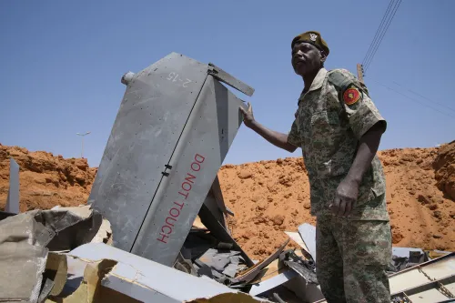 جندي سوداني يقف بجانب حطام طائرة مسيرة في مدينة الأبيض، في سياق الصراع المسلح واستخدام الطائرات المسيّرة في الحرب الأهلية السودانية.